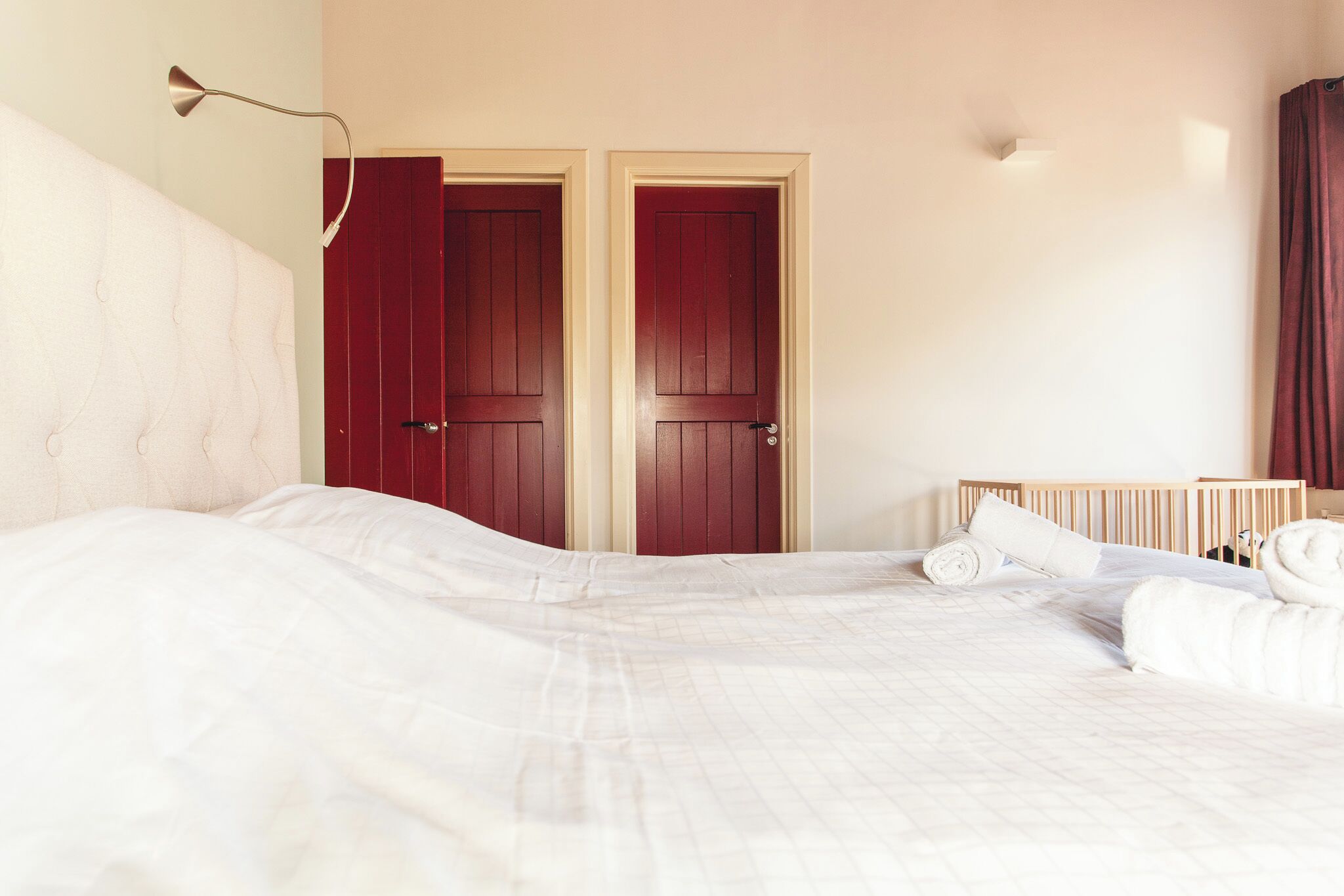 A bedroom with a large bed, two red doors, a wooden headboard, and a bedside lamp.