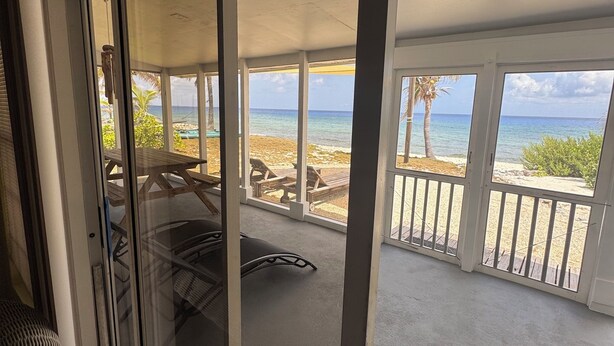 Una habitación con puerta de cristal corredera que da a un balcón con vista a la playa y al océano.