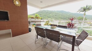 A balcony with a dining table and chairs, potted plants, and a view of a mountainous landscape. - Elegance and comfort for your vacation - apartment with 3 suites at Marine Resort. (Florianópolis)