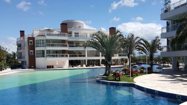 A modern hotel with a large pool, multiple balconies, and palm trees. - Elegance and comfort for your vacation - apartment with 3 suites at Marine Resort. (Florianópolis)