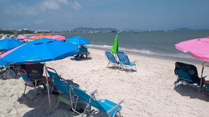A beach with rows of blue and pink beach umbrellas, some with chairs underneath, and a few green umbrellas. - Elegance and comfort for your vacation - apartment with 3 suites at Marine Resort. (Florianópolis)
