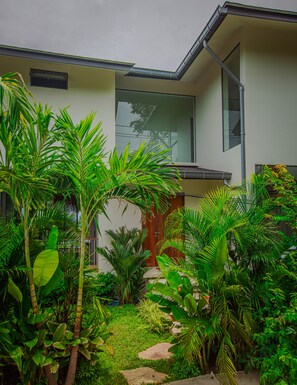 Ein modernes Haus mit einem gepflegten Garten, der verschiedene tropische Pflanzen und einen Kiesweg zeigt.