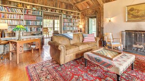 A cozy room with wooden beams, a fireplace, a bookshelf, a leather sofa, and a patterned rug.