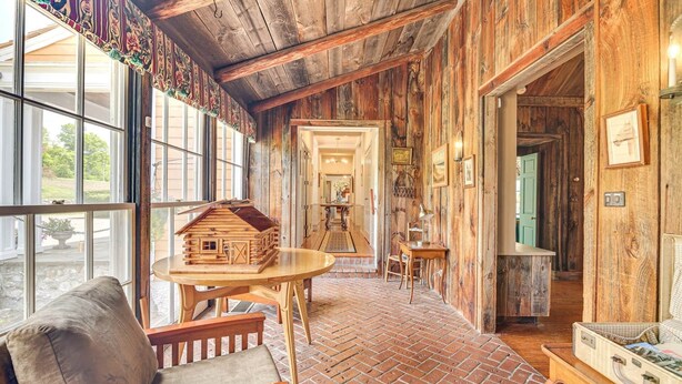 A rustic interior with a brick floor, wooden walls, a wooden table with a model house, and a chair.