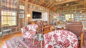 A rustic interior with wooden beams, leather furniture, a bookshelf, and a television.