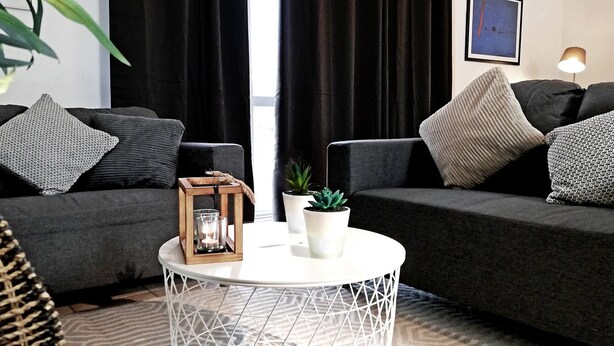 A modern living room with two dark sofas, a round white coffee table, and a small wooden side table with a candle and a plant.