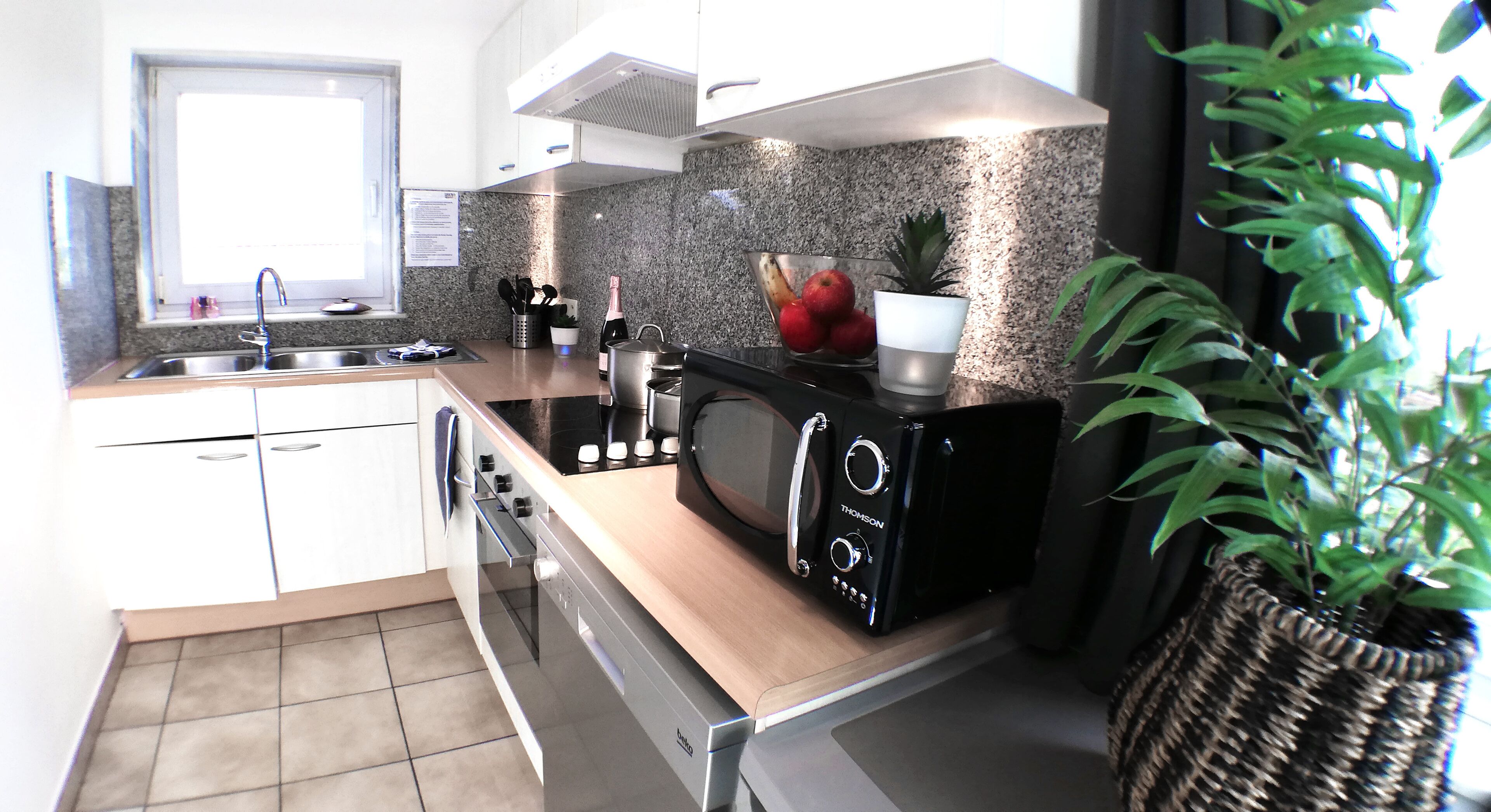 Een moderne keuken met een inbouwoven, magnetron en een roestvrijstalen spoelbak.