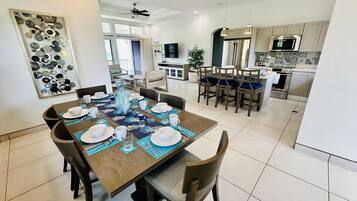A dining area with a wooden table set for four, a kitchen in the background, and a ceiling fan.
