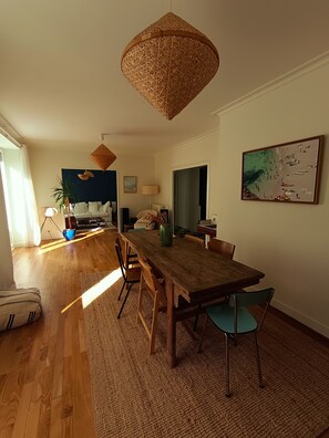 Ein Essbereich mit einem Holztisch und Stühlen, einer gewebten Pendelleuchte und einem großen Gemälde an der Wand.