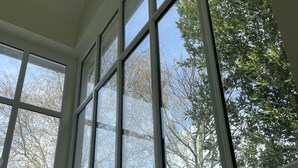Ein Zimmer mit großen Fenstern, einer weißen Tür und freiem Blick auf Bäume.