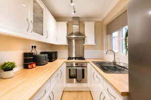 Una cocina moderna con gabinetes blancos, una campana extractora de acero inoxidable, un horno empotrado, un fregadero y un ventanal que proporciona luz natural.