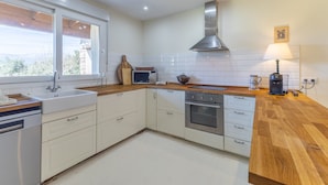 Cocina moderna con armarios blancos, extractor de acero inoxidable, encimera de madera y ventana con vistas.