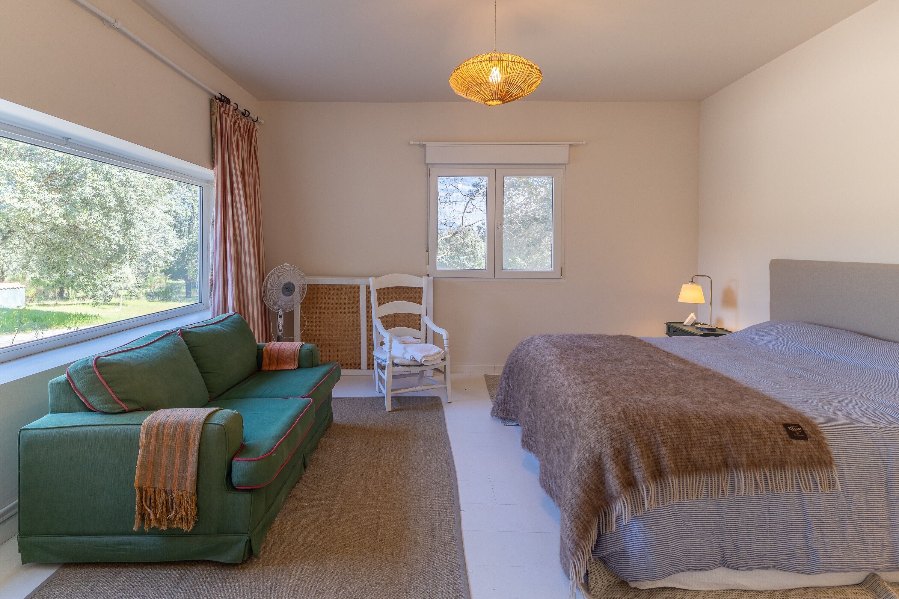 Un dormitorio con cama, sofá verde, silla, ventana y ventilador de techo.