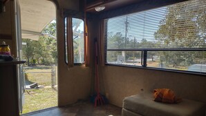 Ein Zimmer mit großem Fenster, einer Couch, einem Besen und einem kleinen Tisch mit einem Glas.