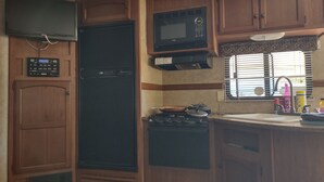 Eine kompakte Küchenzeile für Wohnmobile mit Kühlschrank, Mikrowelle, Herd und Spüle mit Fenster darüber.
