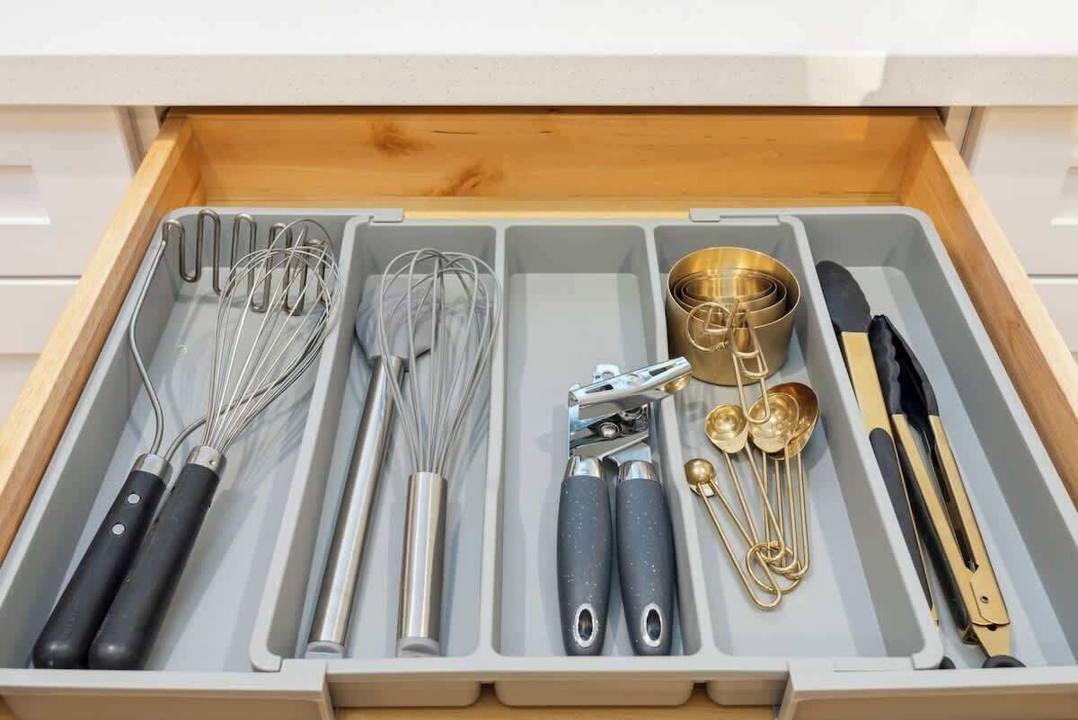 A drawer containing kitchen utensils including whisks, a grater, measuring spoons, and a knife.