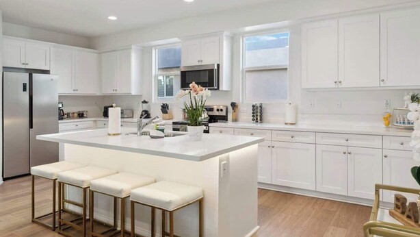 A modern kitchen with white cabinetry, a central island with bar stools, stainless steel appliances, and a large window providing natural light. - Family-Friendly Retreat, 20min to Disney & OC (Santa Ana)