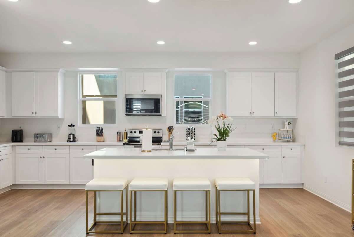 A modern kitchen with white cabinetry, a central island with bar stools, a microwave, and a large window.