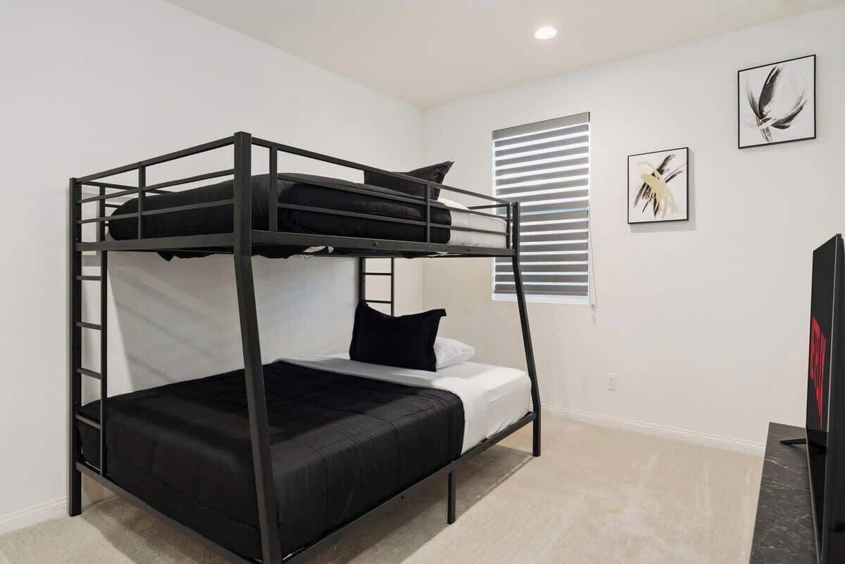 A bunk bed room with a ladder, a window with blinds, and two framed artworks on the wall.