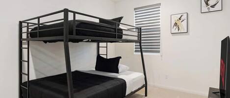 A bunk bed room with a ladder, a window with blinds, and two framed artworks on the wall.
