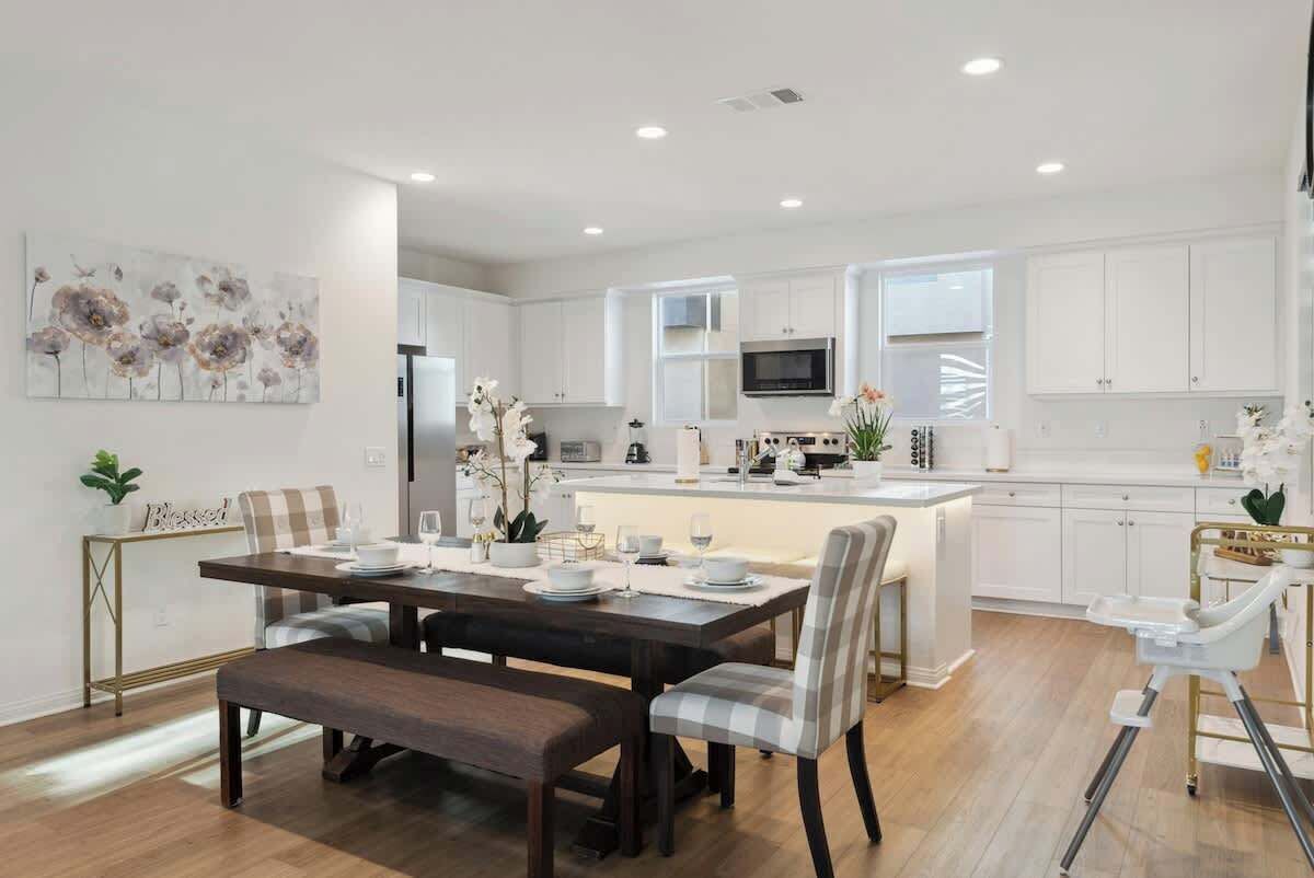 A modern kitchen with white cabinets, a central island, and a dining area with a bench and chairs.