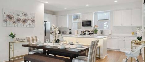 A modern kitchen with white cabinets, a central island, and a dining area with a bench and chairs.