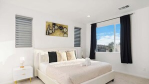 A modern bedroom with a large bed, a bedside table, a window with curtains, and a cityscape view. - Family-Friendly Retreat, 20min to Disney & OC (Santa Ana)