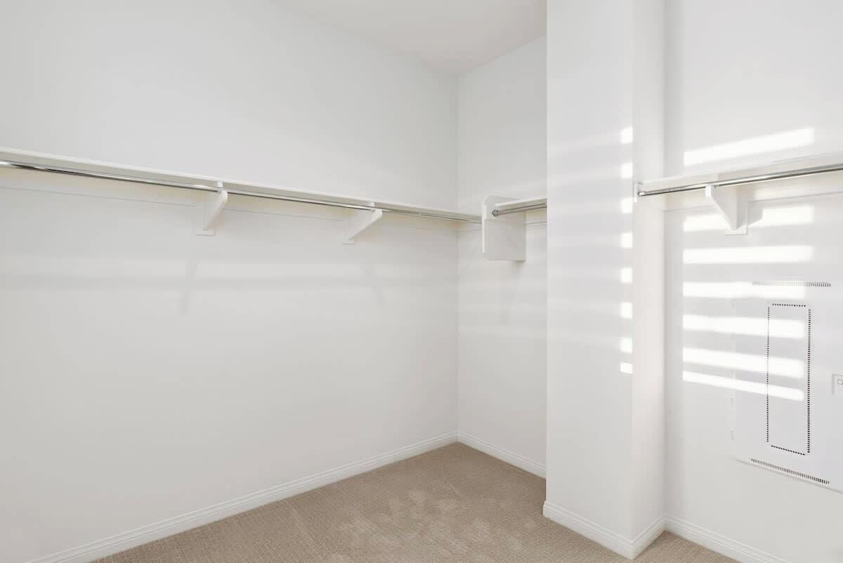 Una habitación con paredes blancas, alfombra color beige y una barra de armario metálica.