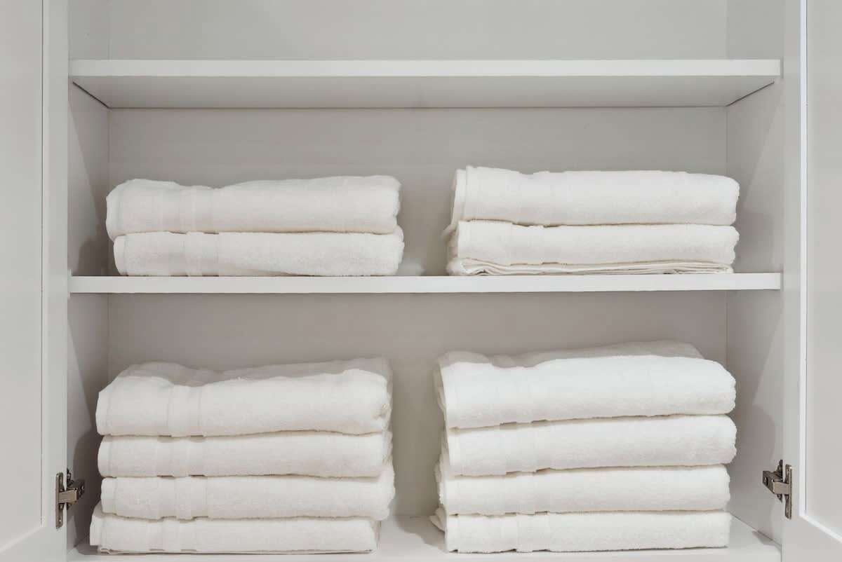 A white wardrobe with two shelves and two drawers, each containing neatly folded white towels.