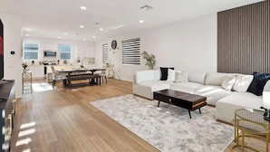 A modern living room with a sofa, coffee table, and a dining area with a table and chairs. - Family-Friendly Retreat, 20min to Disney & OC (Santa Ana)