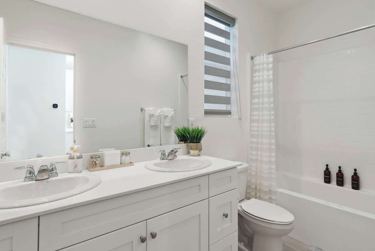 A modern bathroom with two sinks, a large mirror, a toilet, and a shower area.