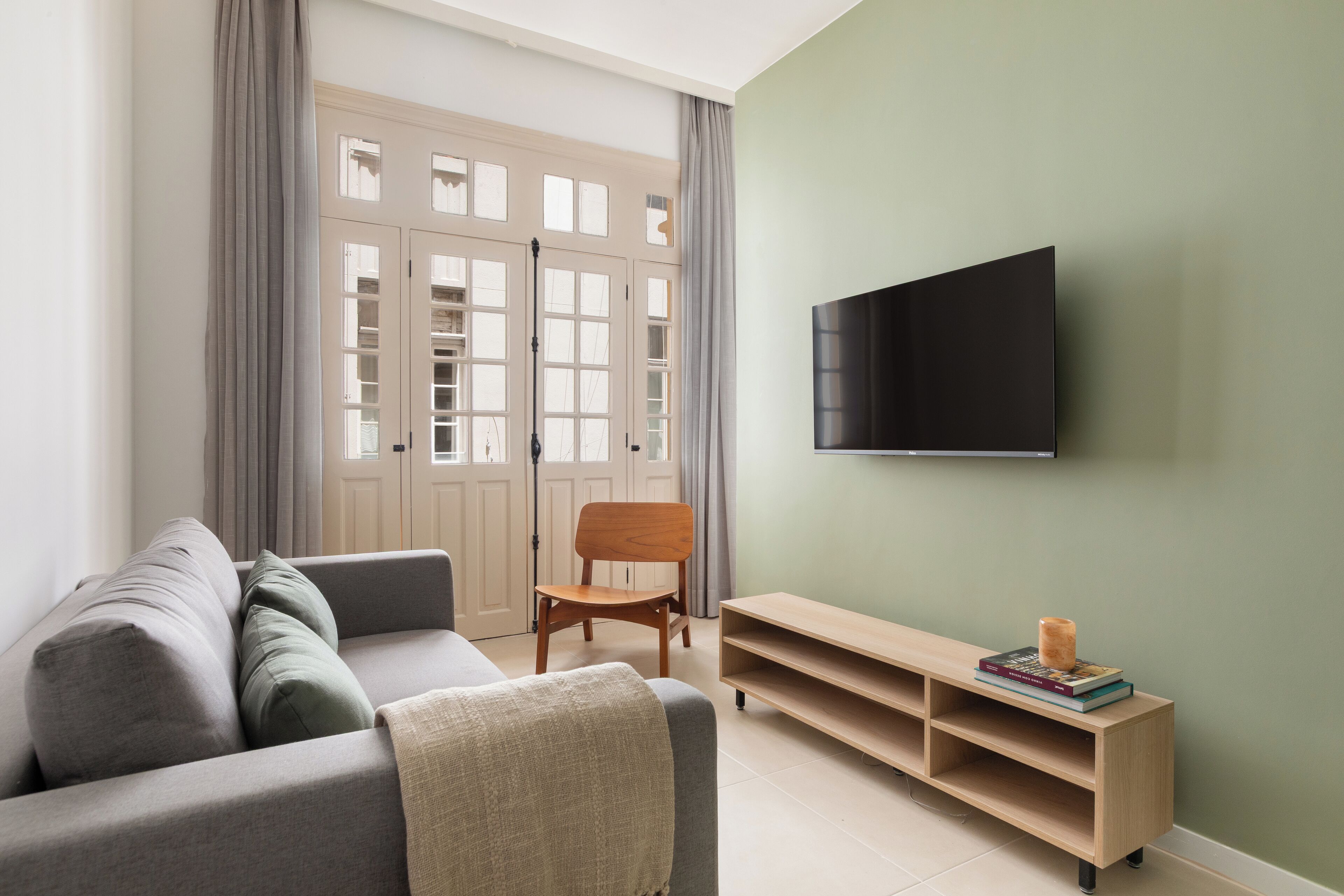 Ett modernt vardagsrum med en grå soffa, en trästol, en TV som är monterad på väggen och en bokhylla.