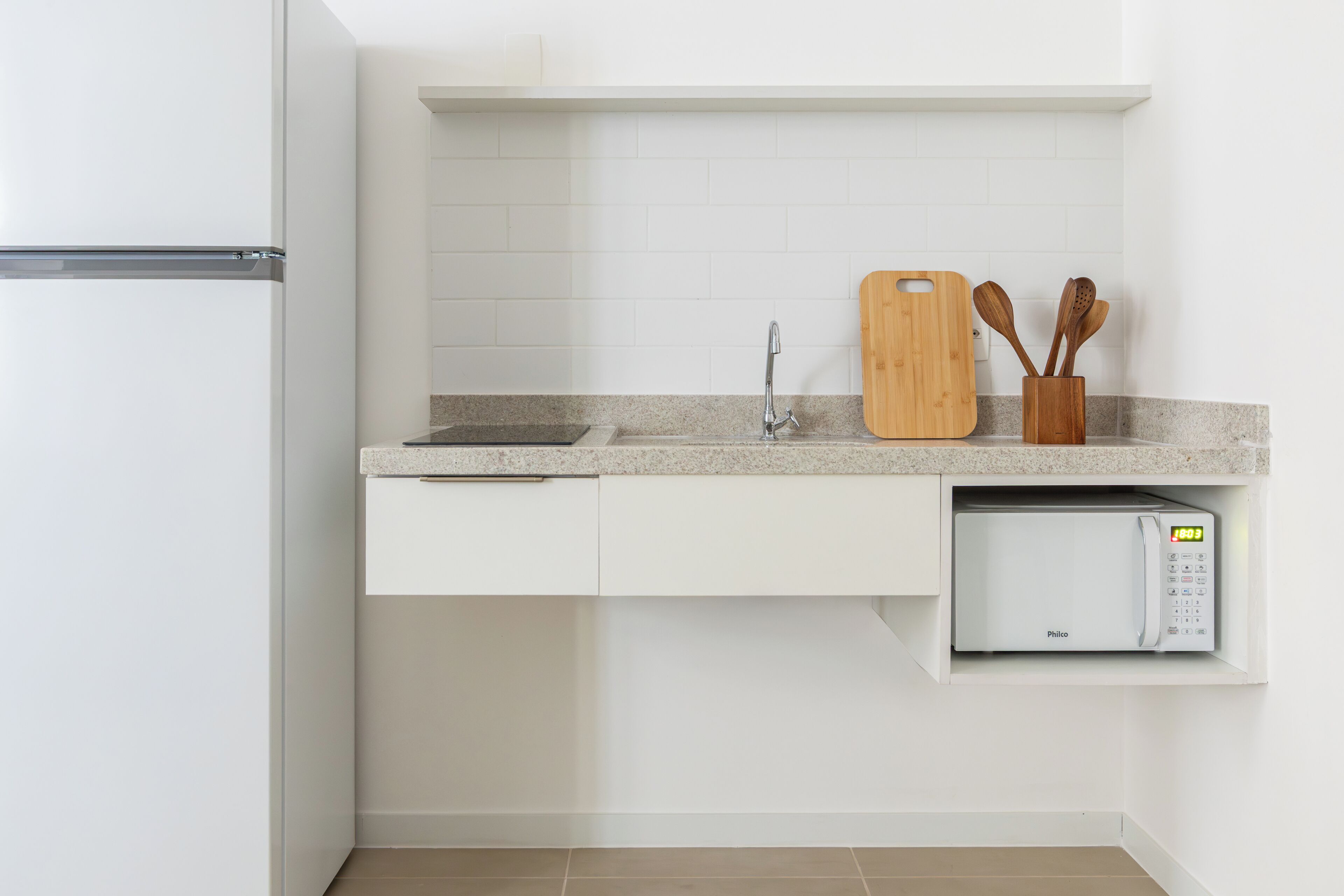 A kitchen with a white refrigerator, a microwave, a wooden cutting board, and wooden utensils on the counter.