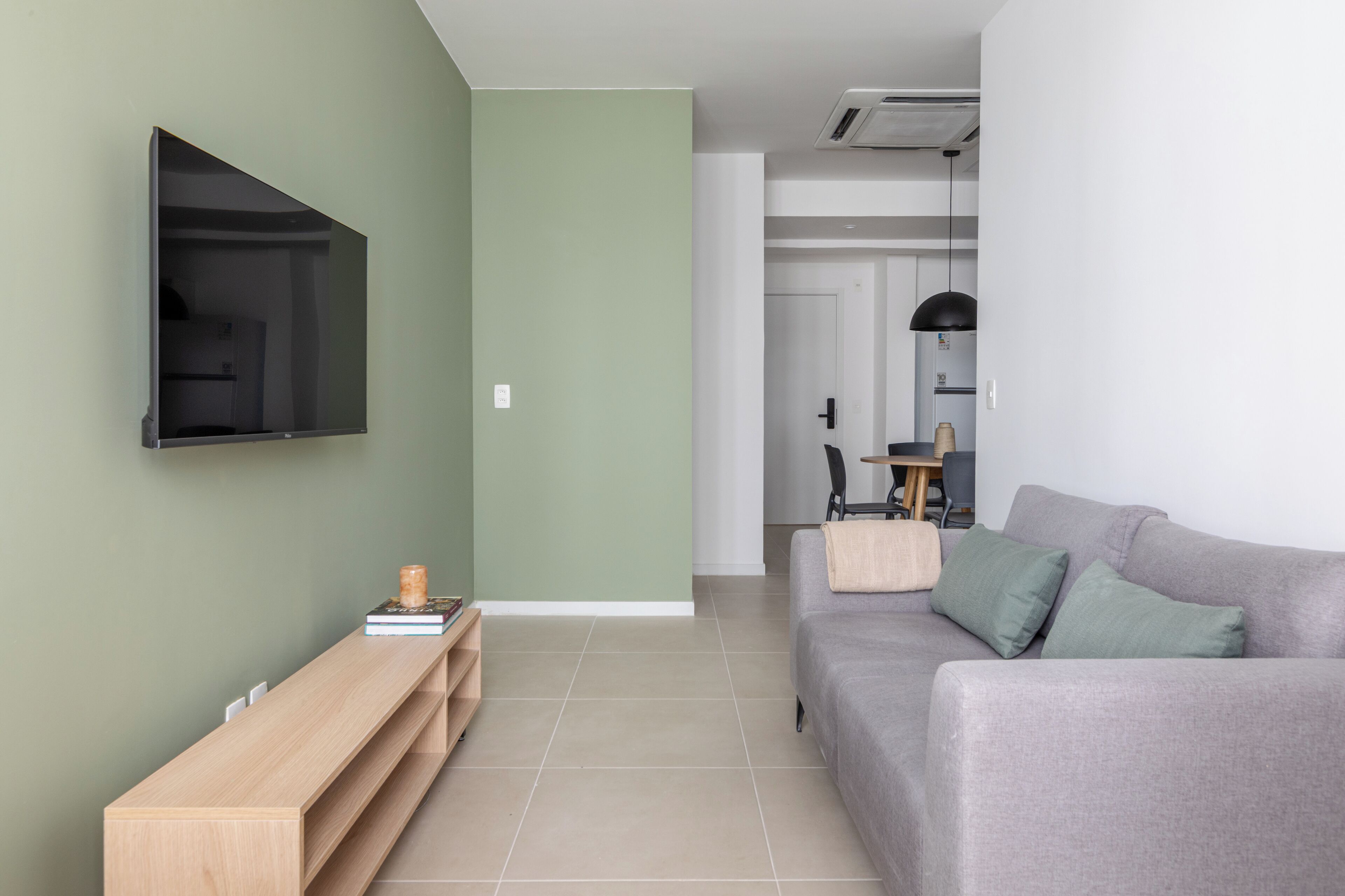 A modern living room with a grey sofa, a wooden TV stand, and a flat-screen TV mounted on the wall.
