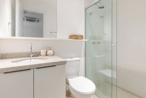 Egy modern fürőszoba üvegfalas zuhanyzóval, fehér mosdókagylóval és WC-vel.