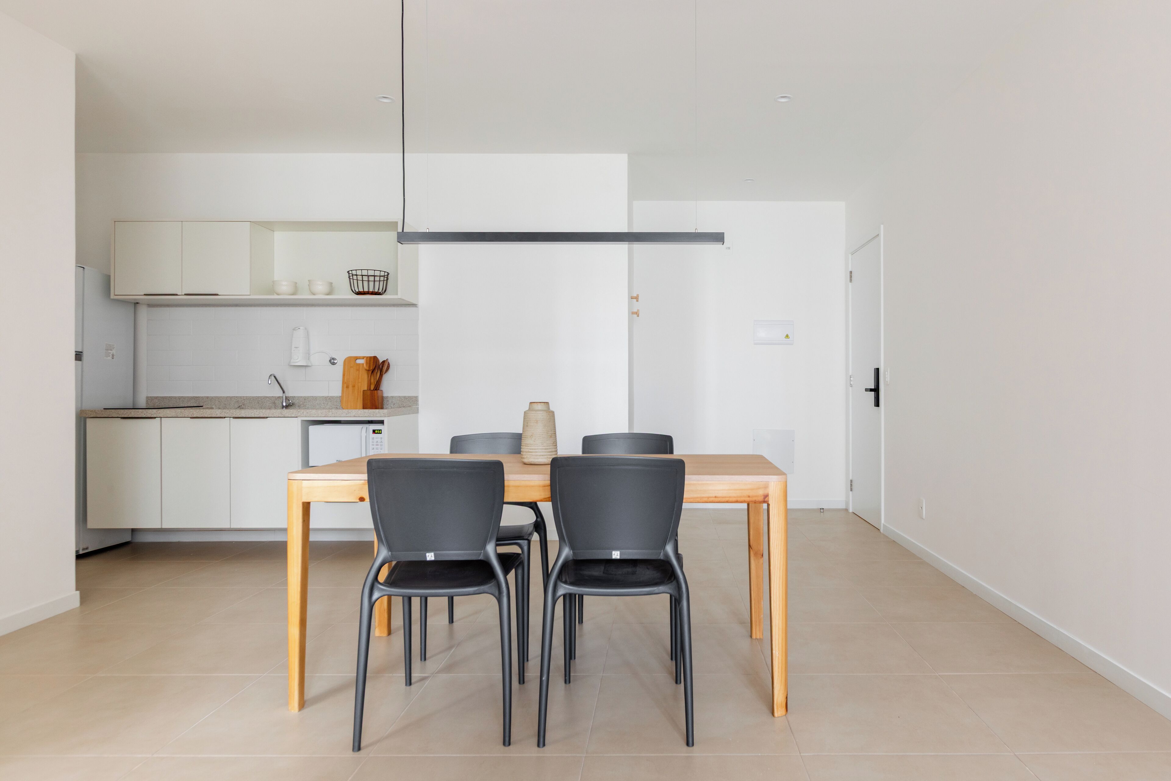 Une cuisine moderne avec des meubles blancs, une table à manger en bois et des chaises noires.