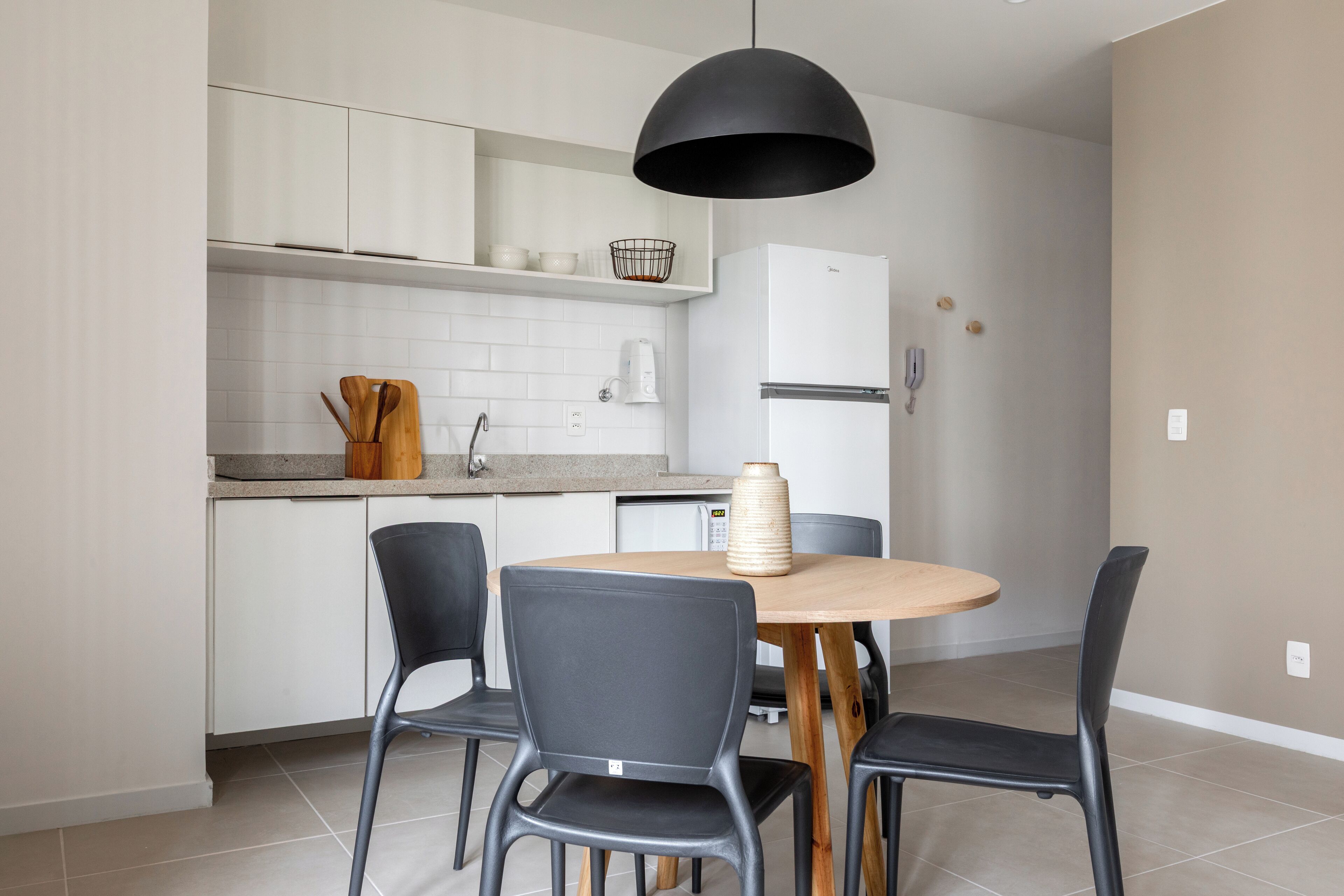 A modern kitchen with white cabinets, a black pendant light, and a round wooden table with four chairs.