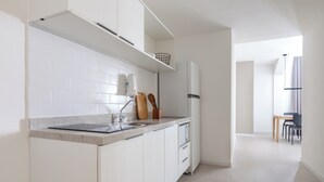 A modern kitchen with white cabinetry, a granite countertop, and a built-in oven. There is a dining area visible in the background with a table and chairs. - Tabas Cena Carioca (Rio de Janeiro)