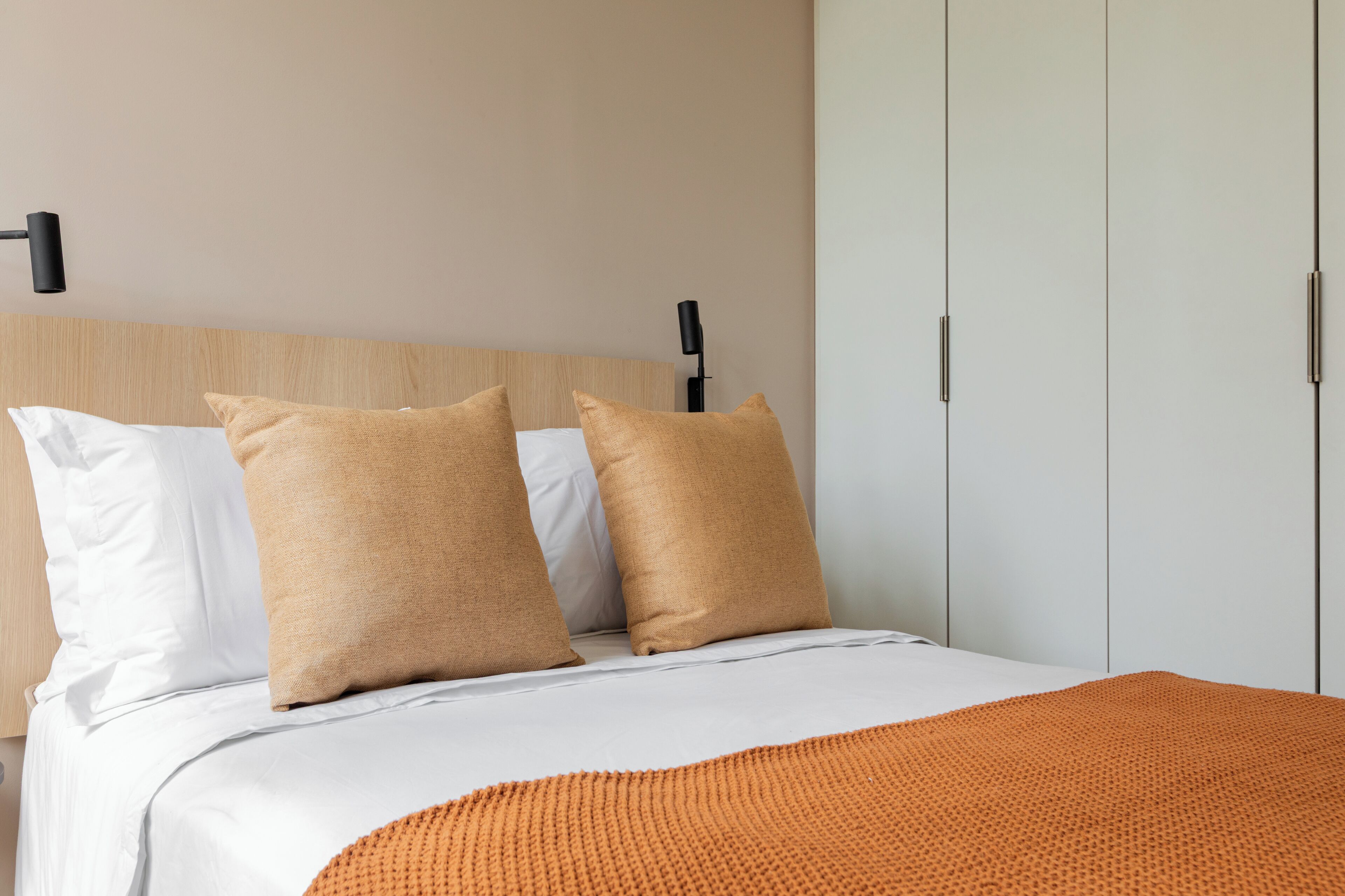 A bed with white and beige pillows, an orange blanket, and a wooden headboard.