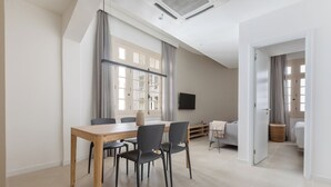 A modern living room with a dining area, a flat-screen TV mounted on the wall, and a large window with curtains. - Tabas Cena Carioca (Rio de Janeiro)
