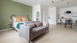 A modern bedroom with a grey sofa, a bed with a wooden headboard, and a small table with a lamp. - Tabas Cena Carioca (Rio de Janeiro)