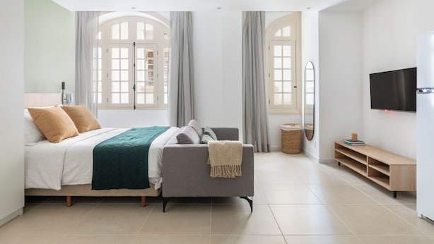 A modern bedroom with a bed, a grey sofa, a TV, and a large window with curtains. - Tabas Cena Carioca (Rio de Janeiro)