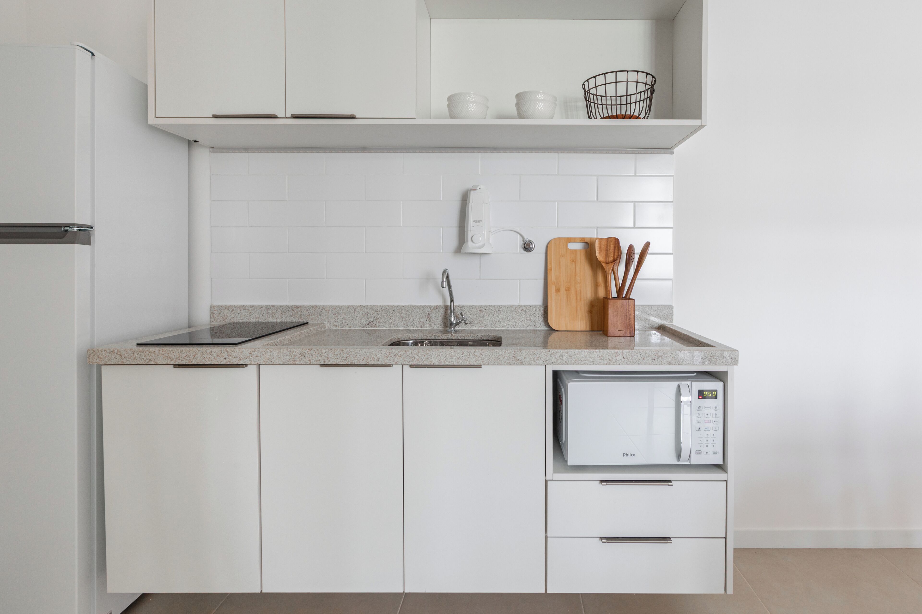 Una cocina moderna con armarios blancos, encimera de granito, microondas integrado y tabla de cortar de madera con utensilios.