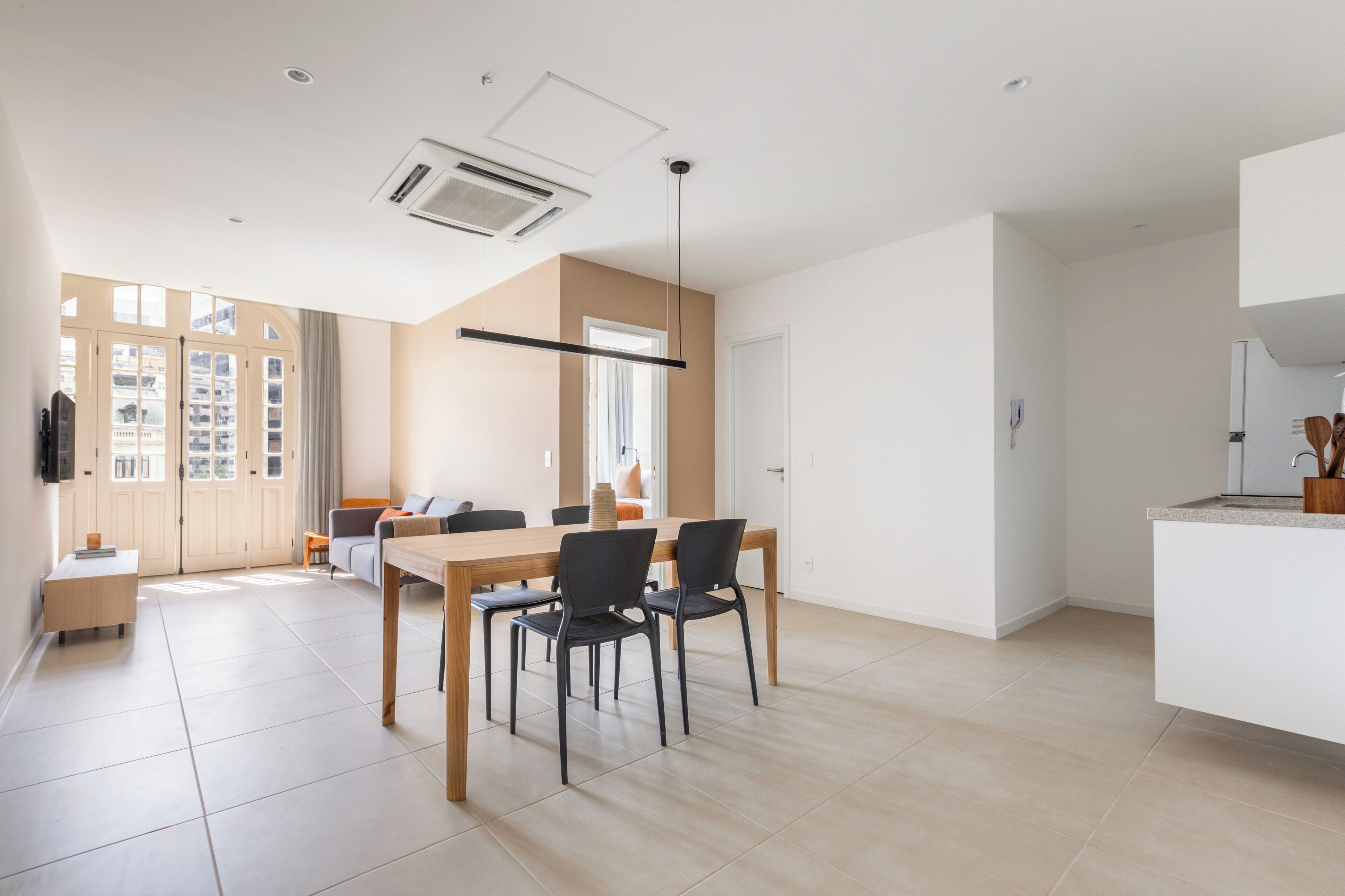 A modern, well-lit living room with a dining area, large windows, and a kitchen.