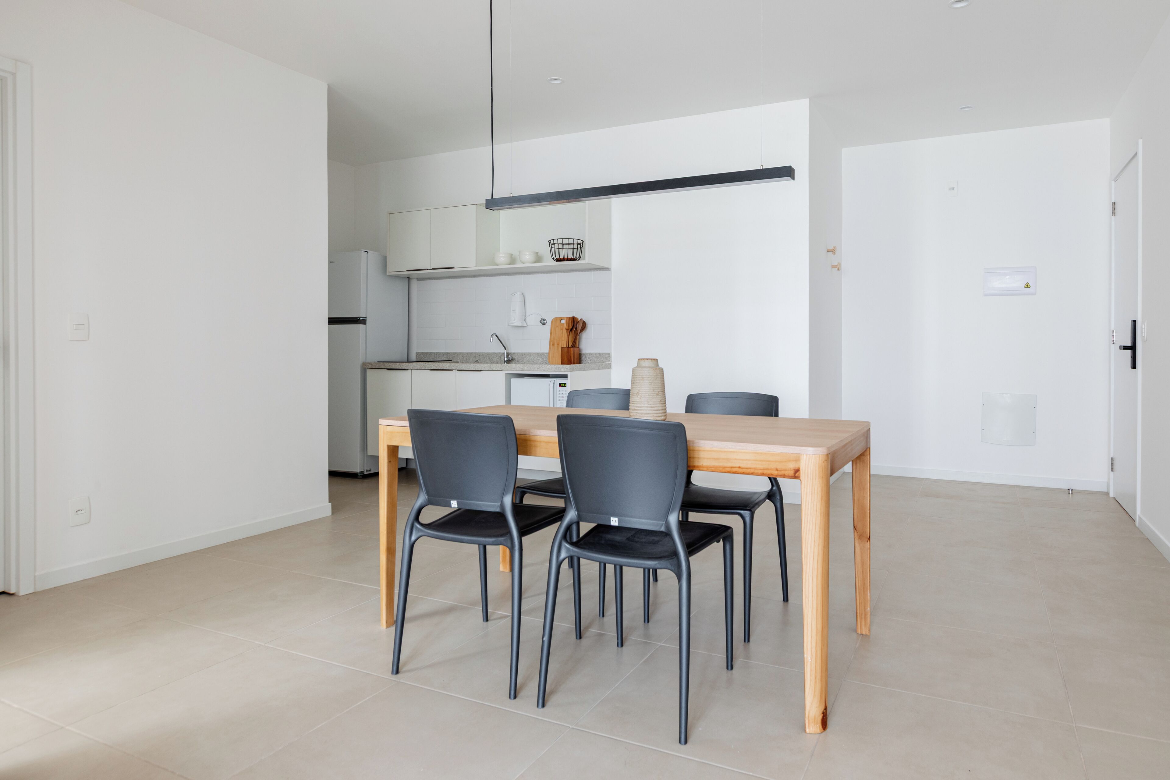A modern kitchen with white cabinets, a wooden dining table, and four black chairs.