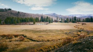 A rural landscape with a small cluster of cabins surrounded by open fields and sparse trees. - Charming Riverside Ranch Retreat with Horse Pasture Views (Bondurant)