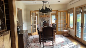 A spacious dining area with a wooden table and chairs, a stone fireplace, and large windows. - Private Pond-Side Manor on a Working Wyoming Ranch (Bondurant)