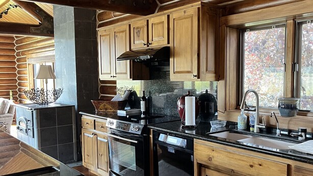 A rustic cabin-style kitchen with wooden cabinets, a large stove, and a window overlooking a forest. - Private Pond-Side Manor on a Working Wyoming Ranch (Bondurant)