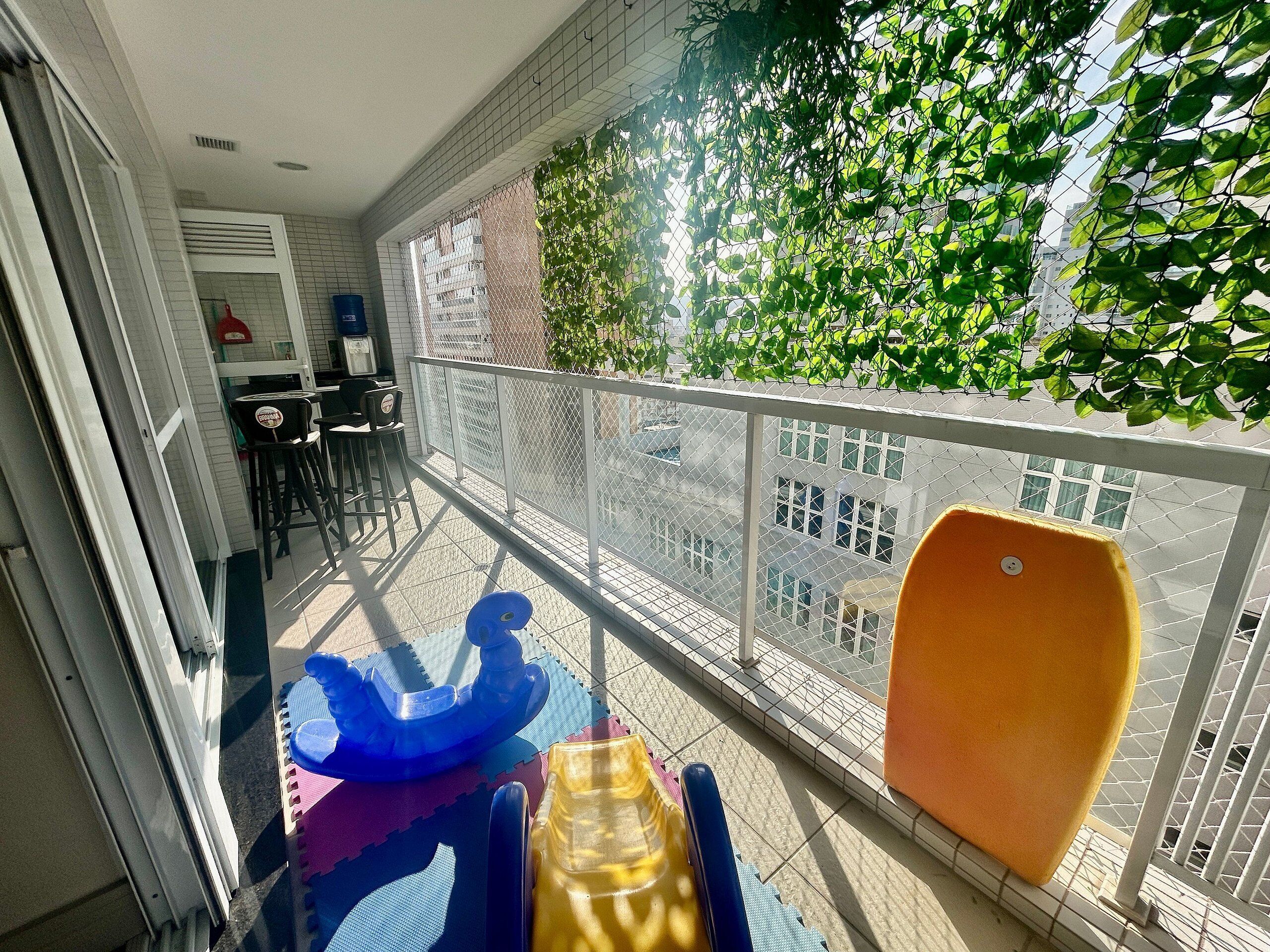 Uma varanda com vista para edifícios, uma mesa com cadeiras e uma cadeira amarela.