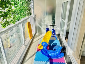A balcony with a safety gate, a yellow object, a blue toy, and colorful interlocking foam mats. - SHB - Complete leisure with pool, sauna at Gonzaga (Santos)